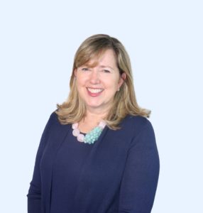 Gail Coote wearing a navy blue shirt and chunky white and aqua colored necklace.