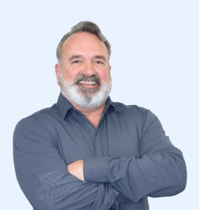 Jim Ward wearing a gray button-up shirt with his arms crossed.