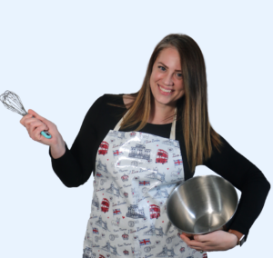 Kellie wearing an apron while holding a whisk and stainless steel mixing bowl.